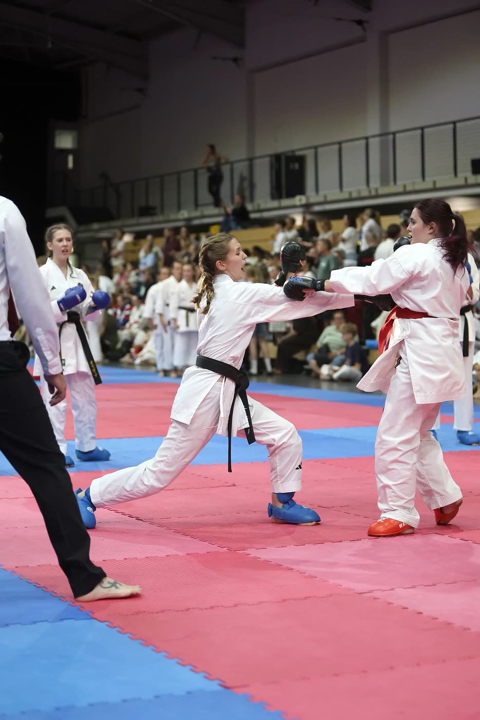 Two junior competitors mid-exchange, one landing a reverse punch, in a kumite bout on the blue and red mats.