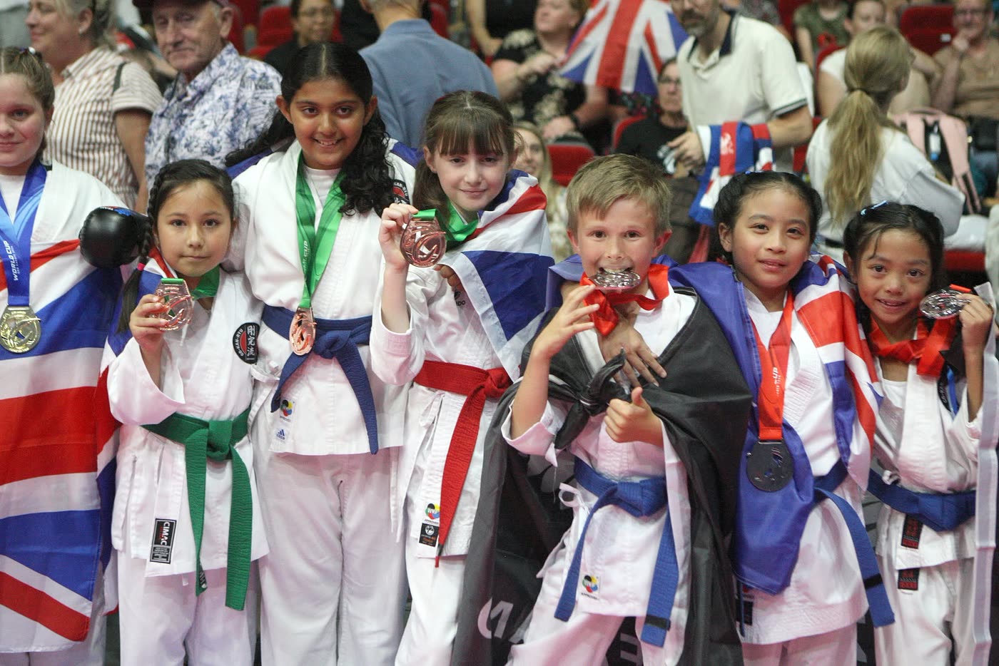 Three young competitors on the podium holding their medals up, draped in flags.